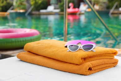 Photo of Beach towels and sunglasses on sun lounger near outdoor swimming pool. Luxury resort