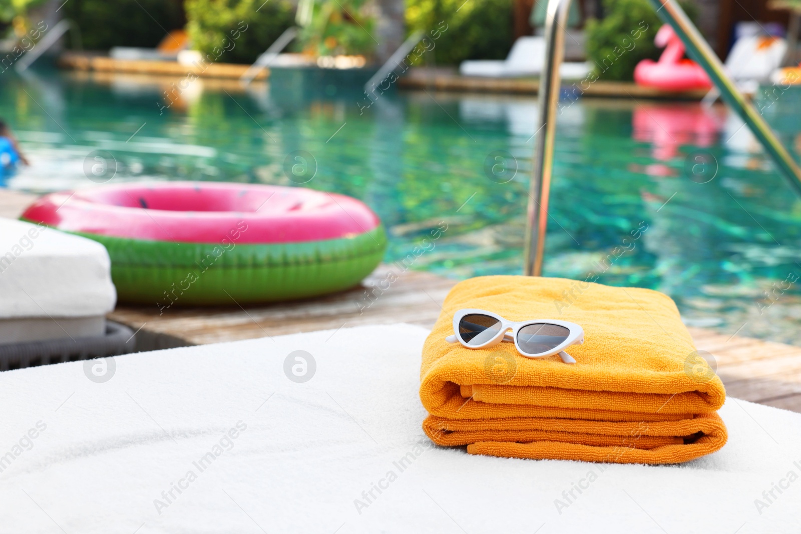 Photo of Beach towels and sunglasses on sun lounger near outdoor swimming pool, space for text. Luxury resort