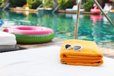 Beach towels and sunglasses on sun lounger near outdoor swimming pool, space for text. Luxury resort