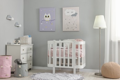 Newborn baby room interior with stylish furniture, comfortable crib and pictures of on wall