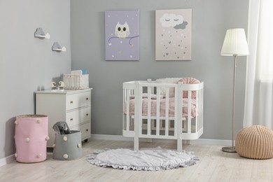 Newborn baby room interior with stylish furniture, comfortable crib and pictures of on wall