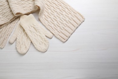 Beige knitted scarf and mittens on white wooden table, top view. Space for text