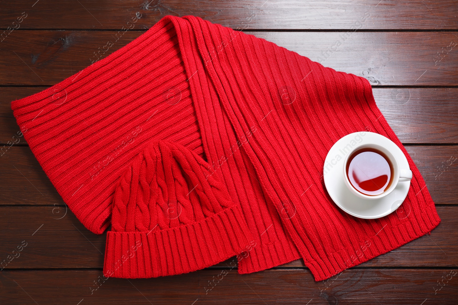 Photo of Knitted scarf, hat and tea on wooden table, top view