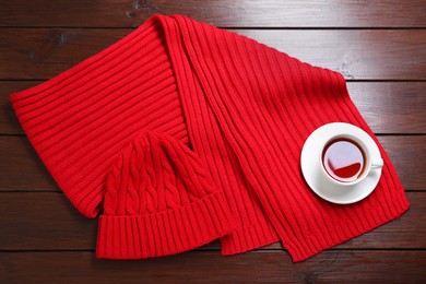 Knitted scarf, hat and tea on wooden table, top view