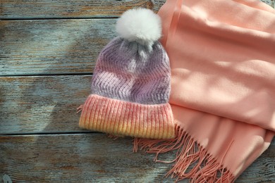 Soft scarf and knitted hat on wooden table, top view. Space for text