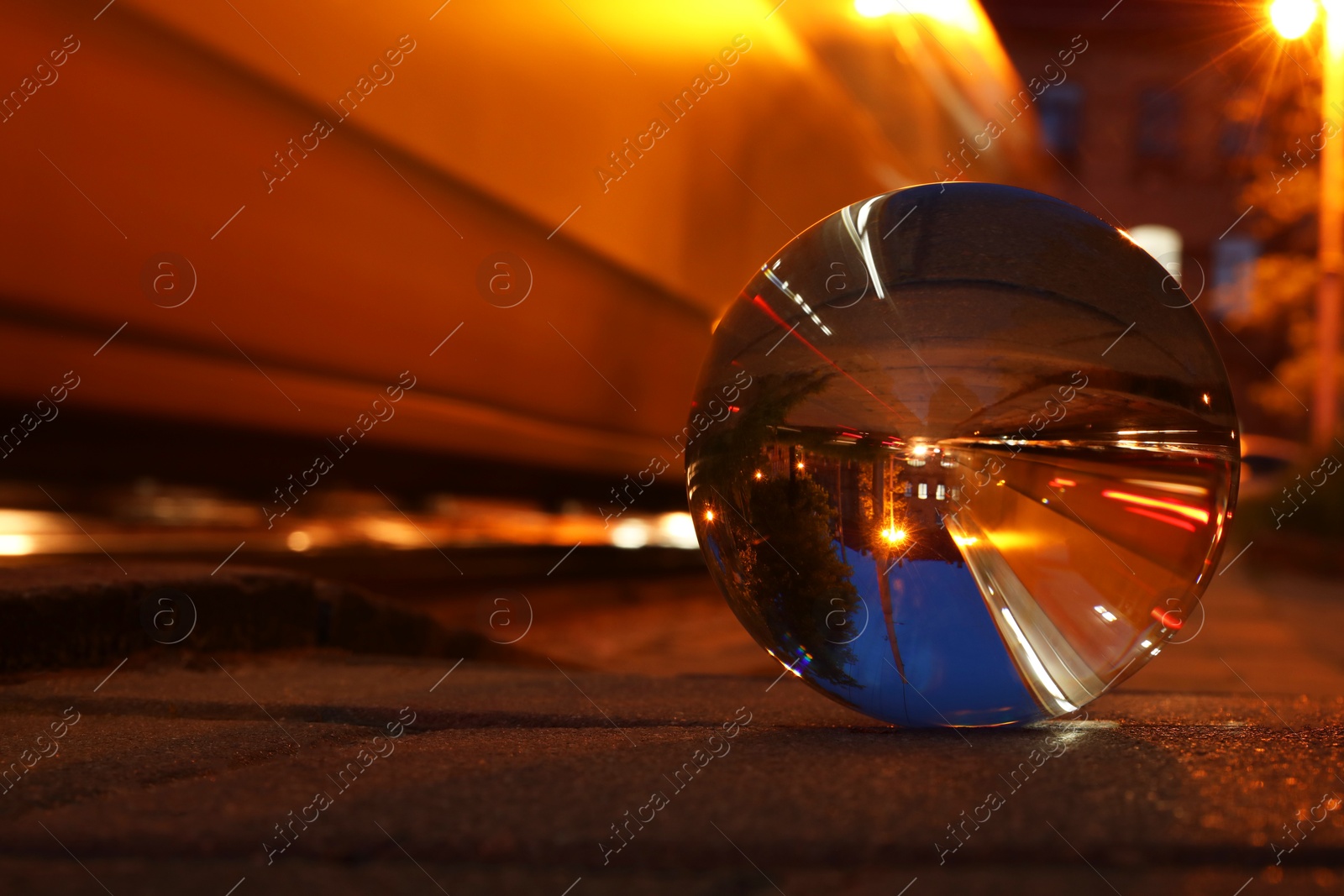 Photo of Beautiful city street, overturned reflection. Crystal ball on asphalt road at night. Space for text