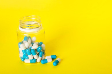 Photo of Antibiotic pills and bottle on yellow background, space for text. Medicinal treatment