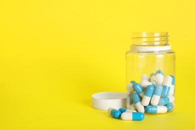 Photo of Antibiotic pills and bottle on yellow background, space for text. Medicinal treatment