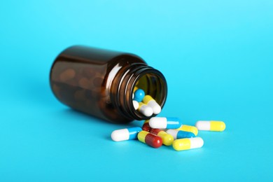 Photo of Scattered antibiotic pills and bottle on light blue background. Medicinal treatment