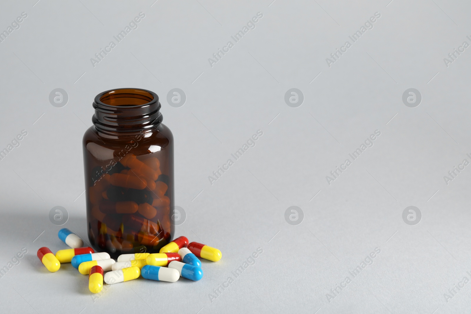 Photo of Antibiotic pills and bottle on grey background, space for text. Medicinal treatment