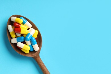 Photo of Many antibiotic pills with wooden spoon and space for text on light blue background, top view. Medicinal treatment