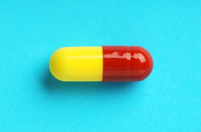 Photo of One antibiotic pill on light blue background, top view. Medicinal treatment