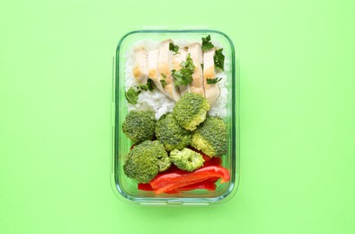 Photo of Healthy meal. Fresh broccoli, pepper, chicken and rice in glass container on green background, top view