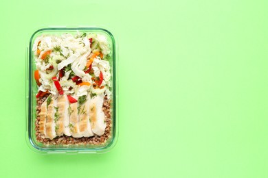 Photo of Healthy meal. Fresh salad, chicken and buckwheat in glass container on green background, top view. Space for text