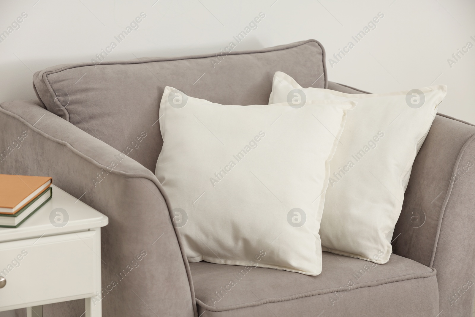 Photo of Soft white pillows on armchair and bedside table near light wall indoors