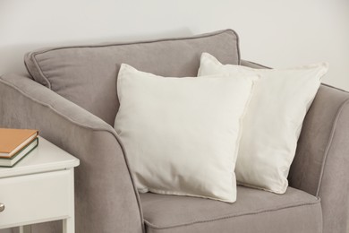 Soft white pillows on armchair and bedside table near light wall indoors