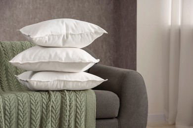 Photo of Stack of soft white pillows on sofa and blanket indoors