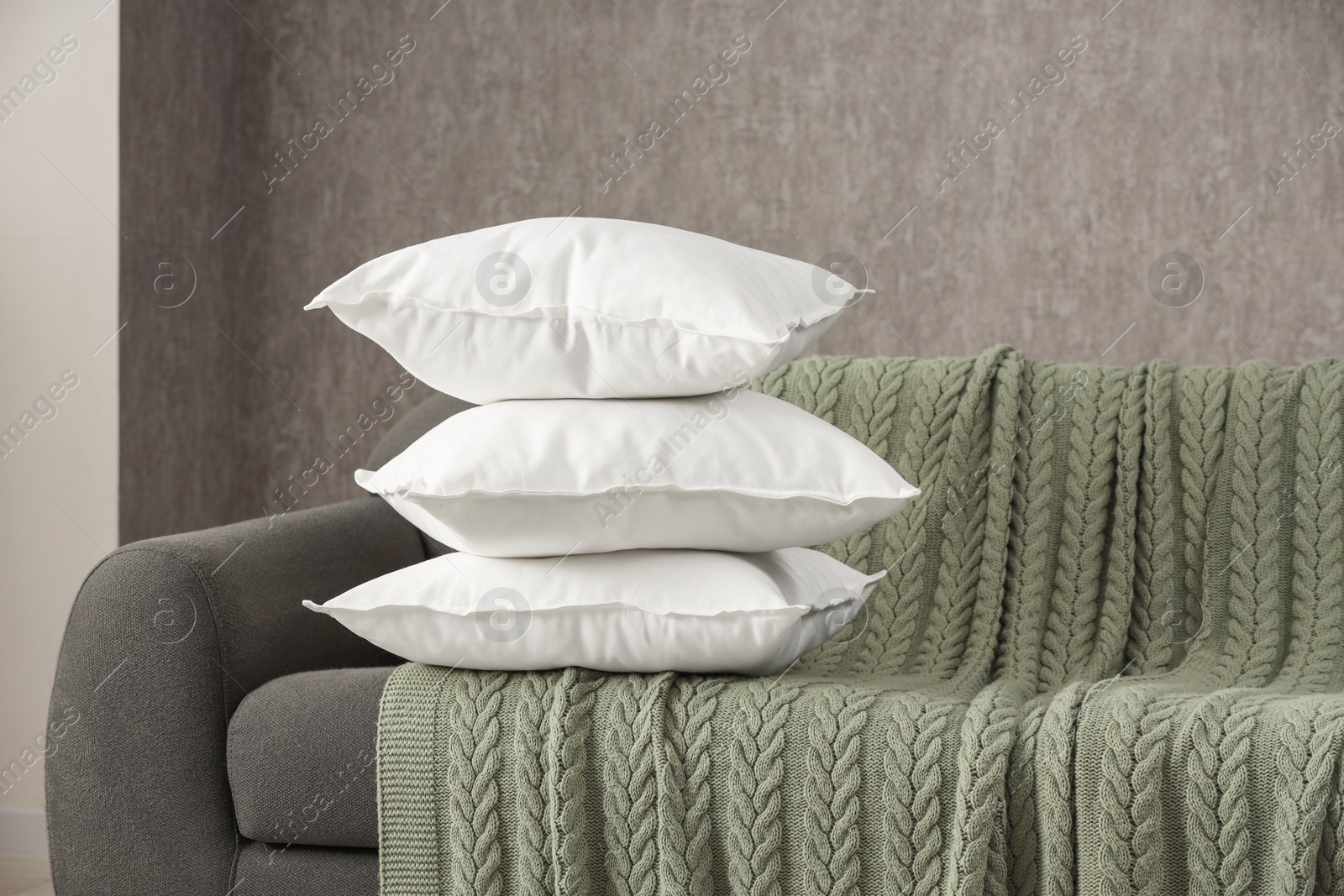 Photo of Stack of soft white pillows on sofa and blanket indoors