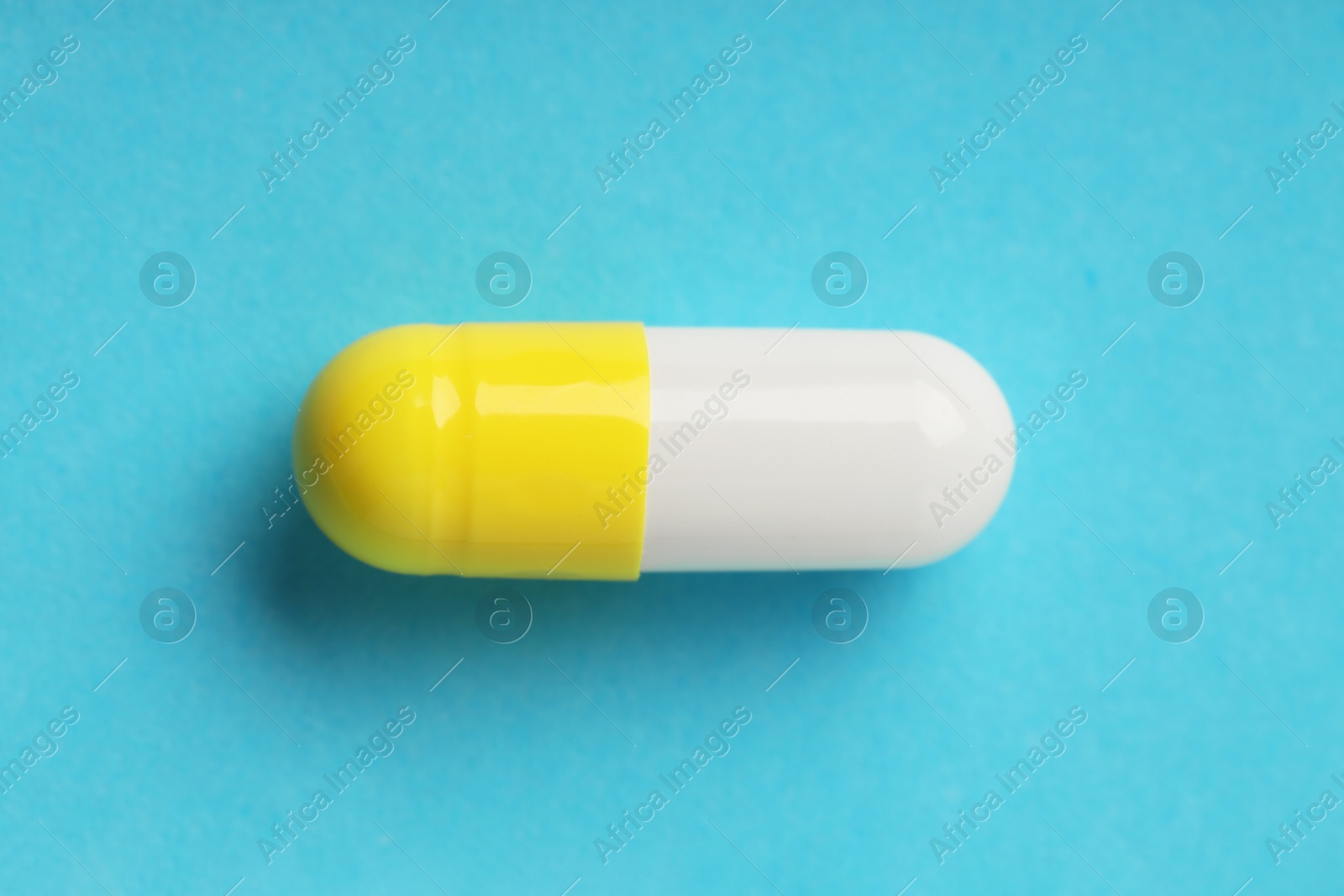 Photo of One antibiotic pill on light blue background, top view. Medicinal treatment