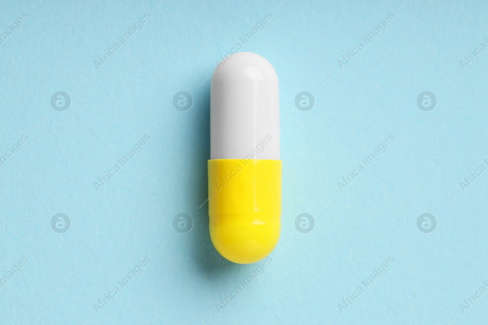 Photo of One antibiotic pill on light blue background, top view