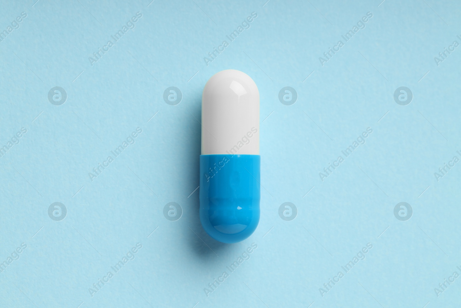 Photo of One antibiotic pill on light blue background, top view