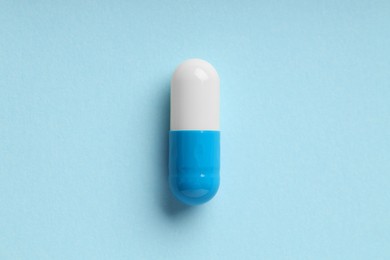 One antibiotic pill on light blue background, top view