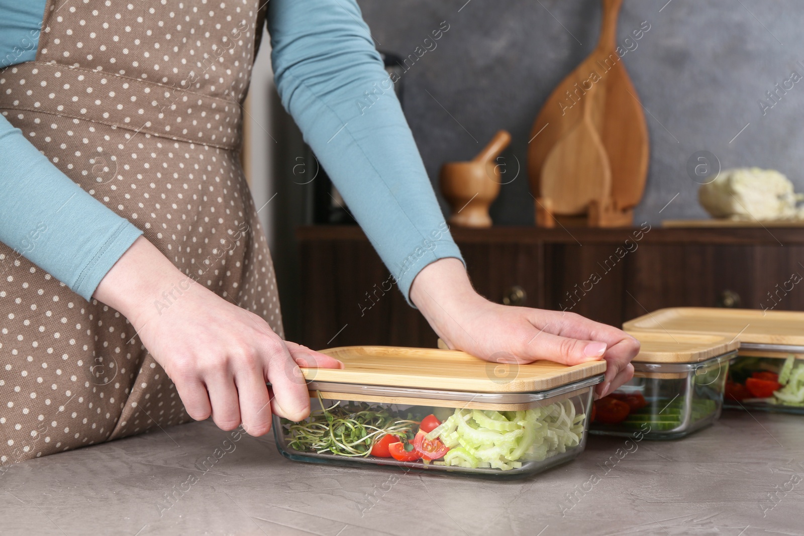 Photo of Healthy food. Woman closing glass container with fresh vegetables at grey table, closeup