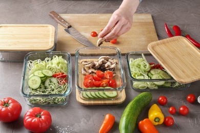 Healthy food. Woman putting pieces of champignons into glass container at grey table, closeup