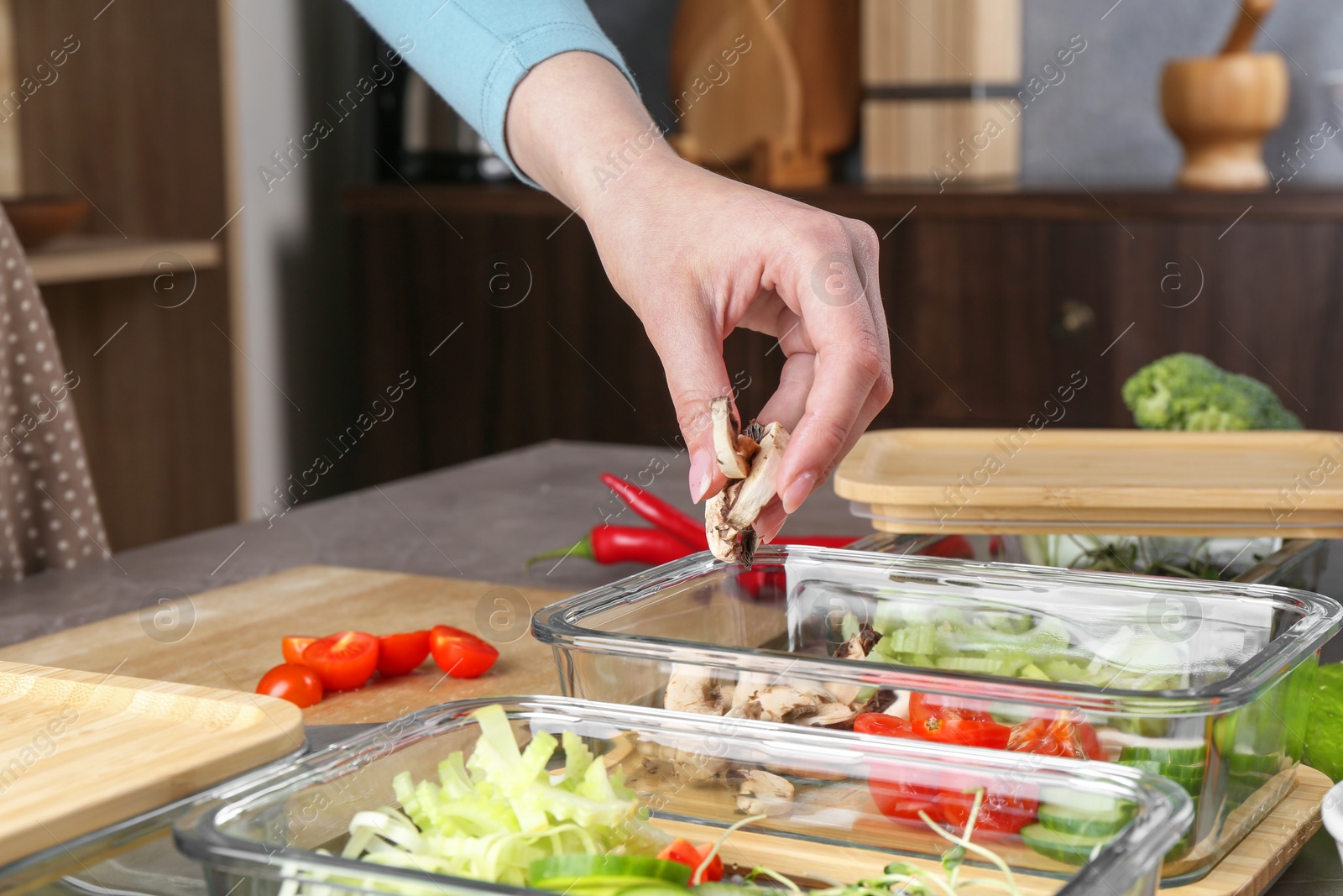 Photo of Healthy food. Woman putting pieces of champignons into glass container at grey table in kitchen, closeup