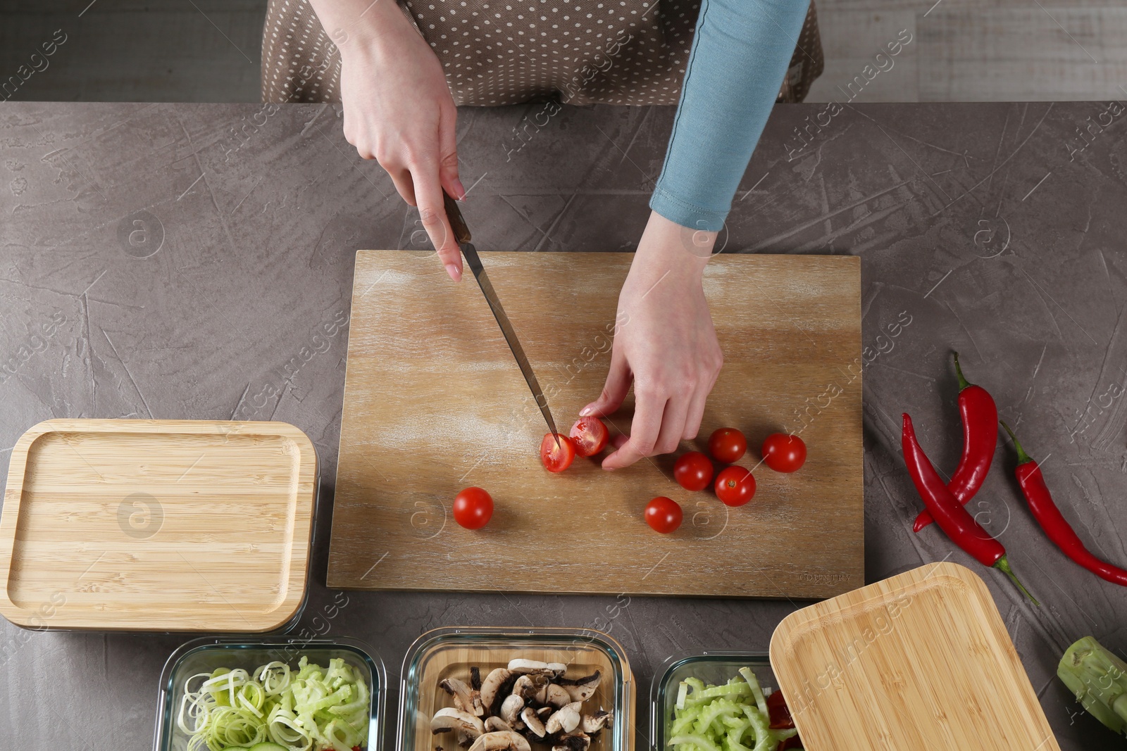 Photo of Healthy food. Woman cutting tomatoes at grey table, top view