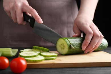 Photo of Healthy food. Woman cutting cucumber at black wooden table, closeup