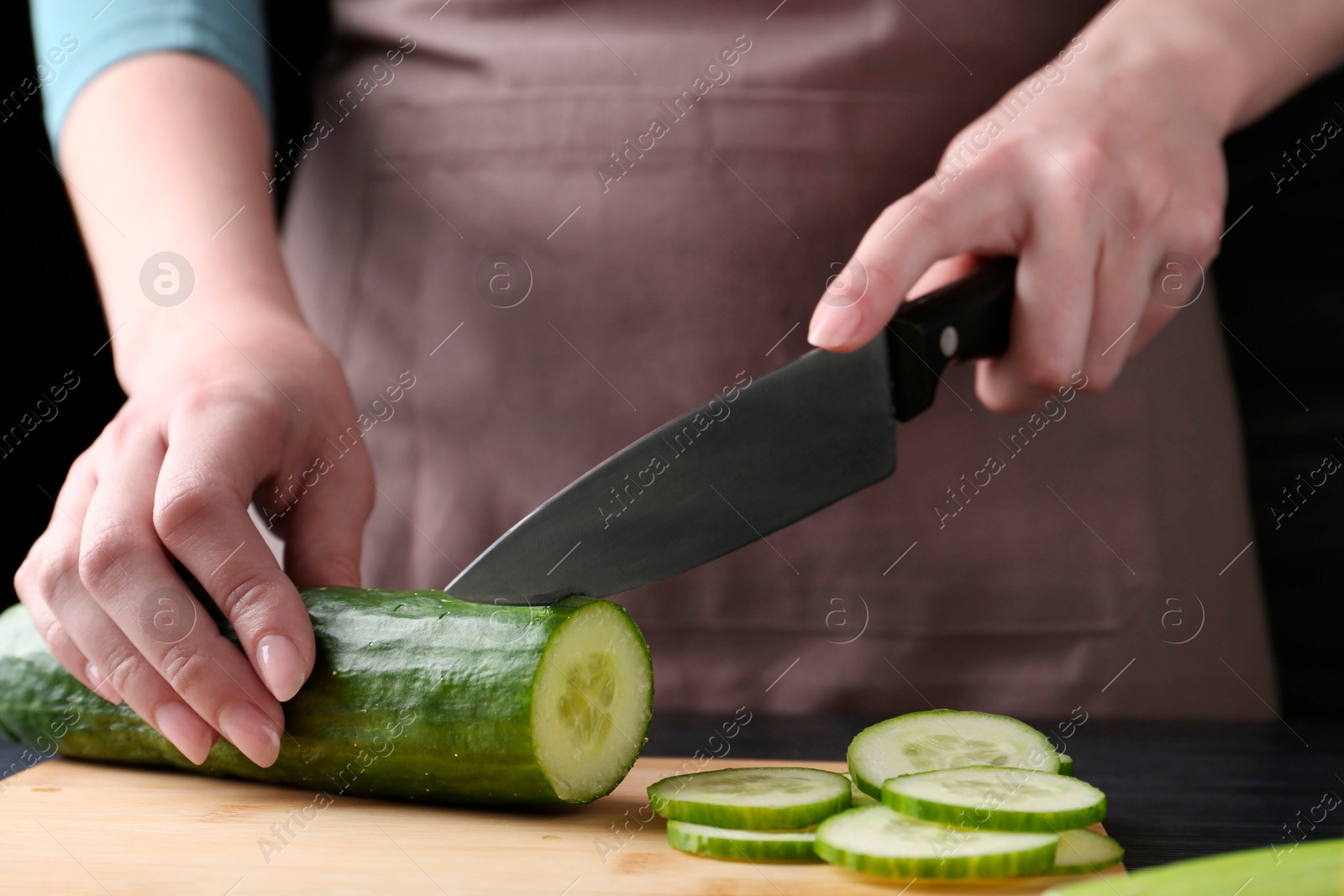 Photo of Healthy food. Woman cutting cucumber at black wooden table, closeup