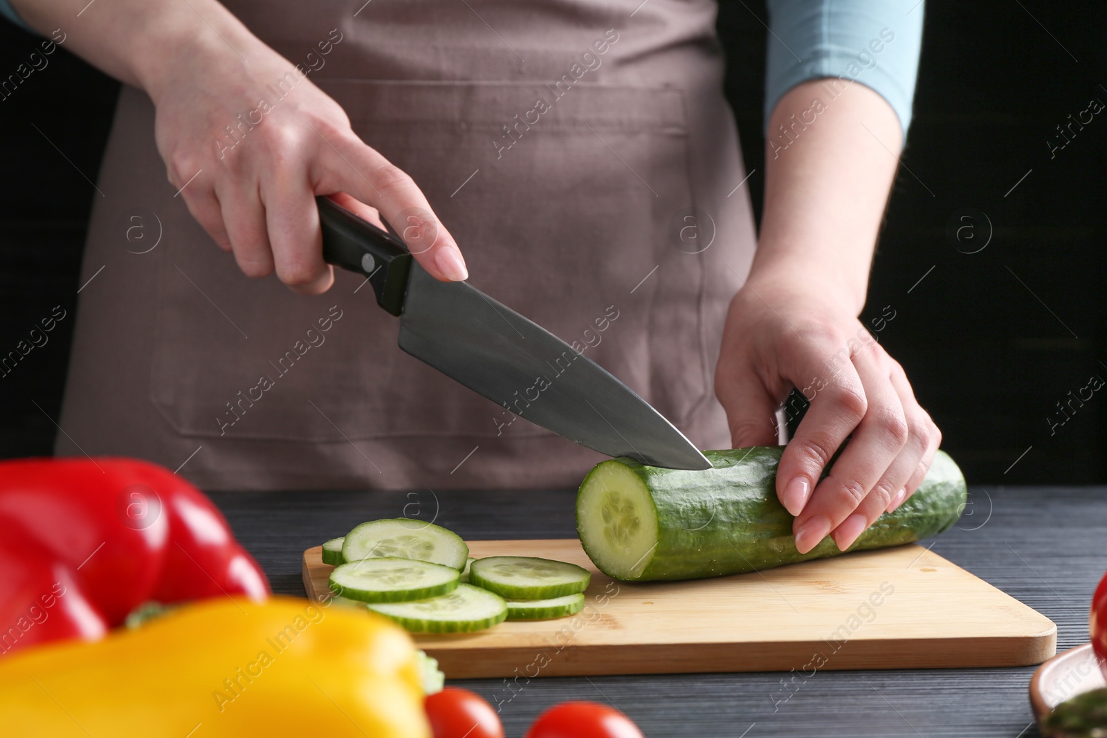 Photo of Healthy food. Woman cutting cucumber at black wooden table, closeup