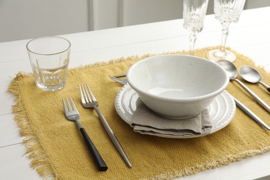 Stylish setting with cutlery, dishes, glasses and napkin on white wooden table