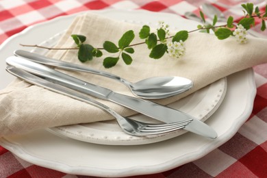 Stylish setting with cutlery, plates, napkin and floral decor on table, closeup