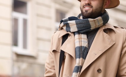 Photo of Smiling man in warm scarf on city street, closeup. Space for text