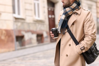 Smiling man in warm scarf with paper cup outdoors, closeup. Space for text