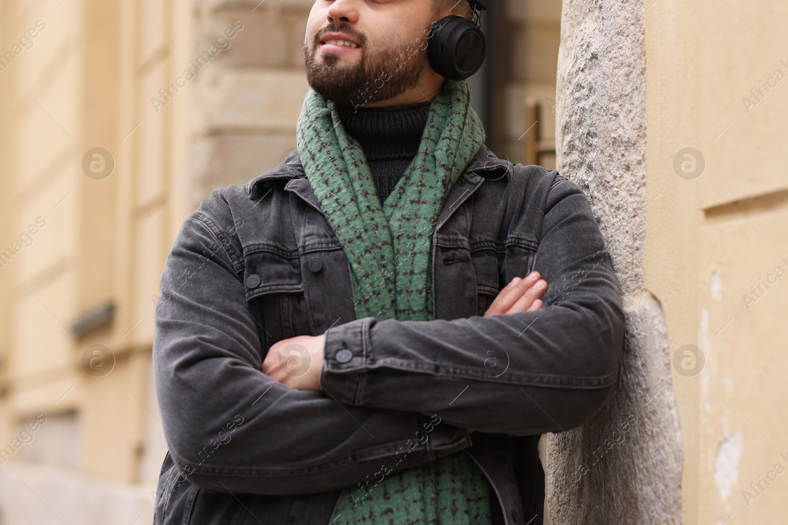 Photo of Smiling man in warm scarf and headphones near building outdoors, closeup