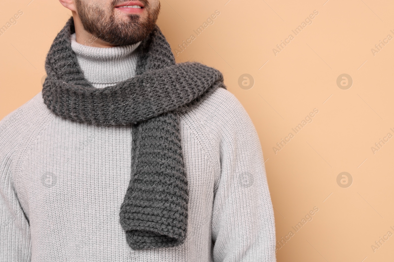 Photo of Smiling man in knitted scarf on beige background, closeup. Space for text