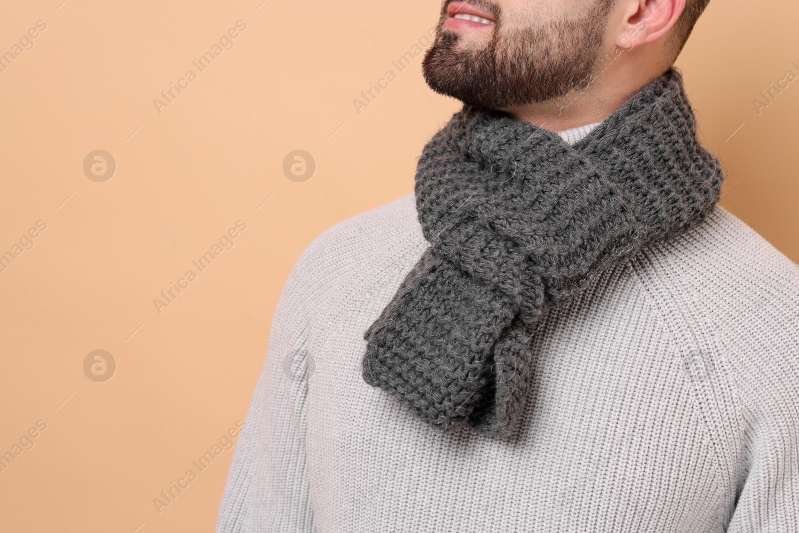 Photo of Smiling man in knitted scarf on beige background, closeup. Space for text