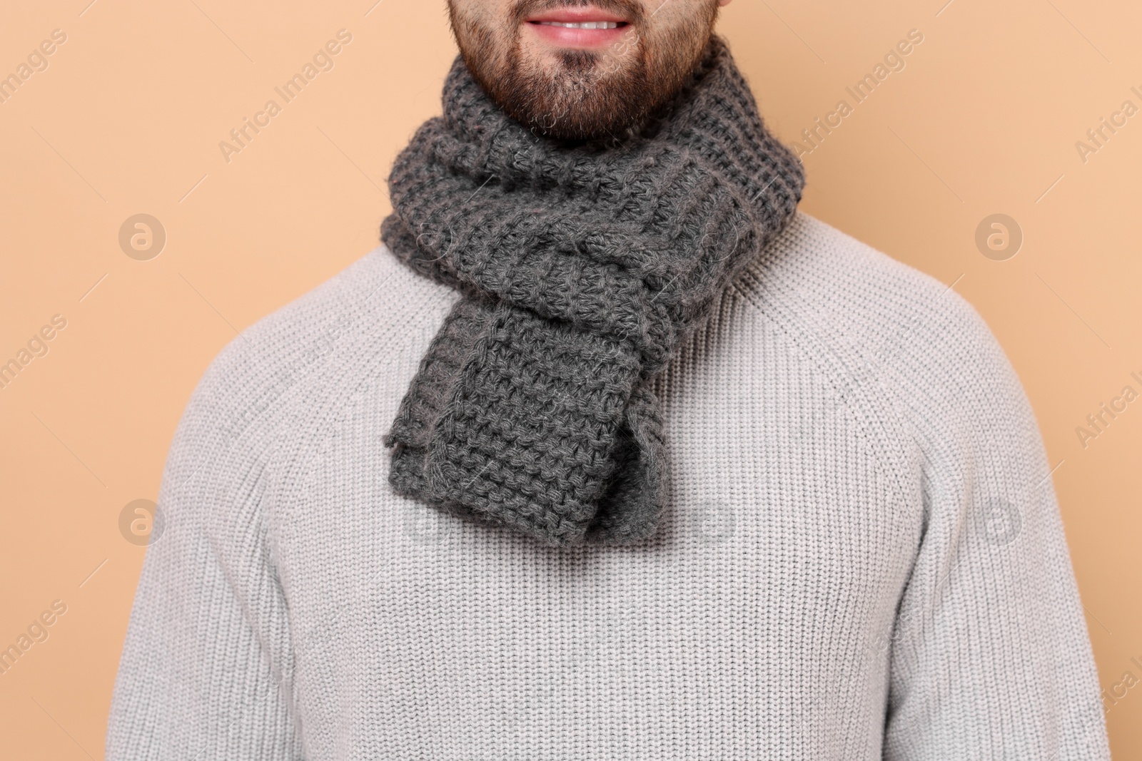 Photo of Smiling man in knitted scarf on beige background, closeup