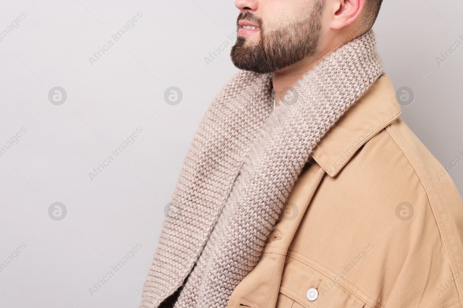 Photo of Smiling man in warm scarf on light grey background, closeup. Space for text