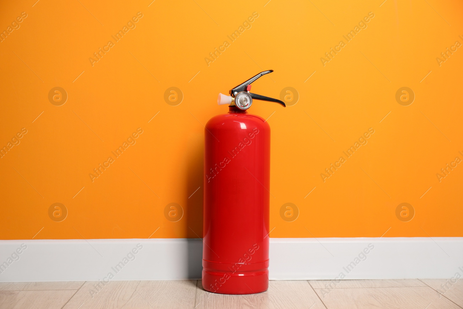 Photo of Fire extinguisher on floor near orange wall