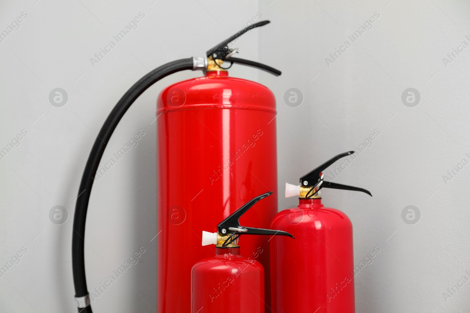 Photo of Three fire extinguishers near light grey wall