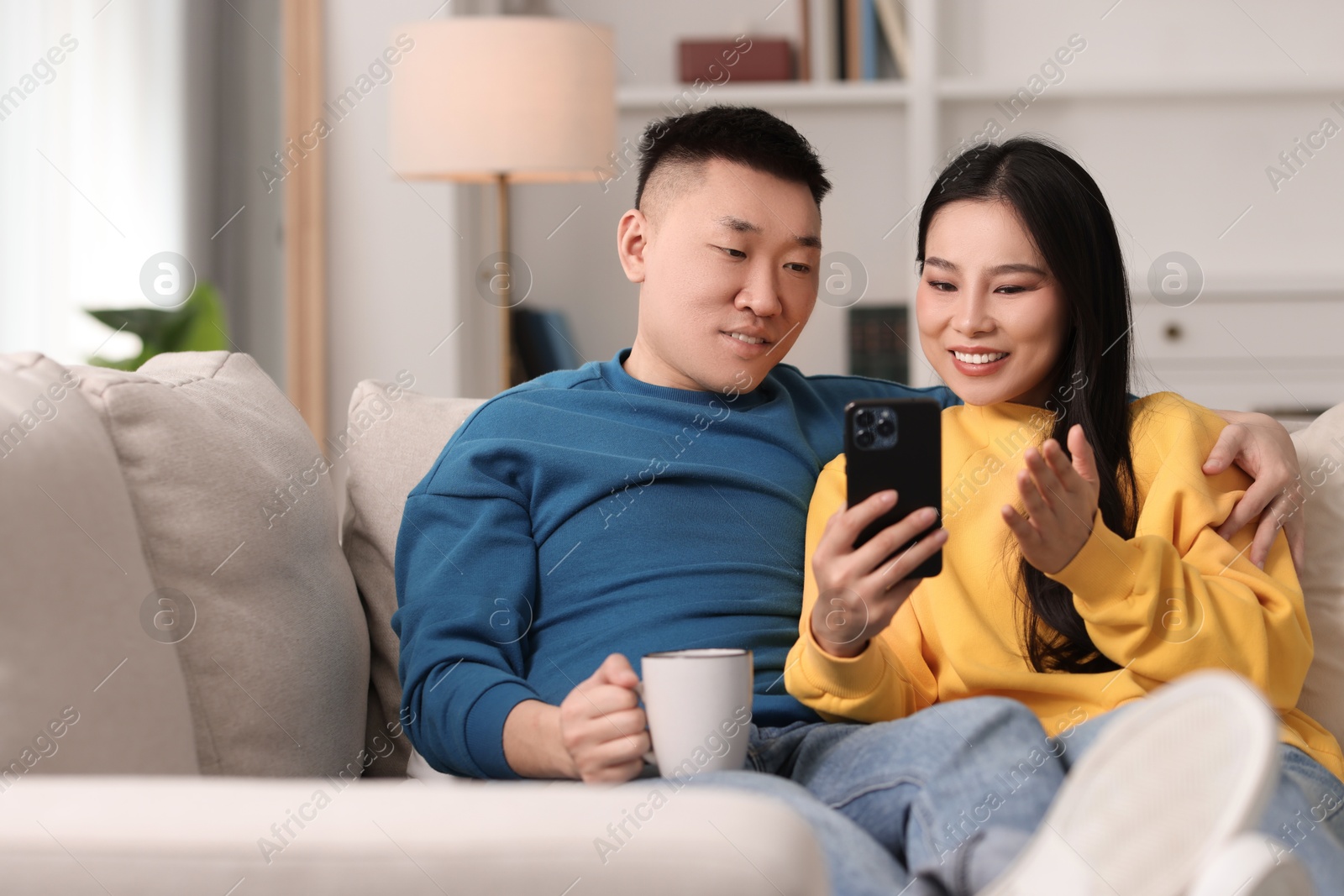 Photo of Happy couple with smartphone on sofa at home