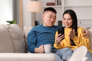 Photo of Happy couple with smartphone on sofa at home