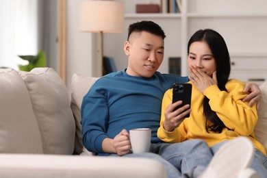 Photo of Happy couple with smartphone on sofa at home