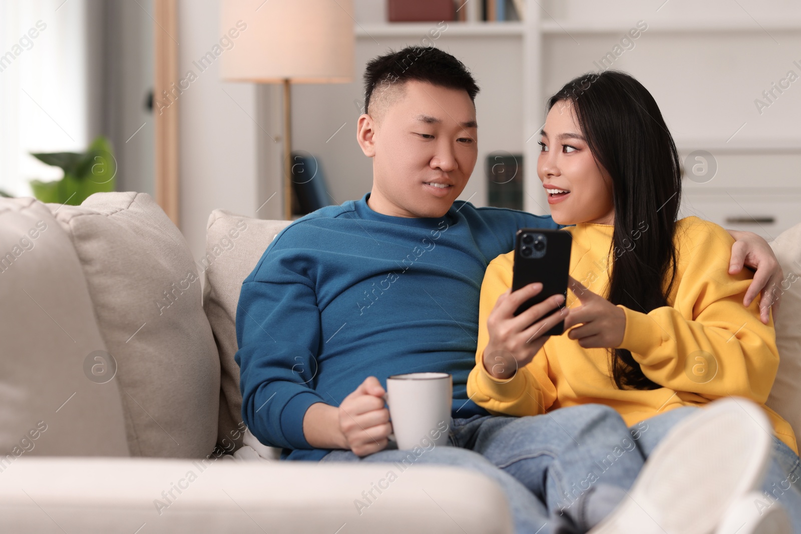 Photo of Happy couple with smartphone on sofa at home