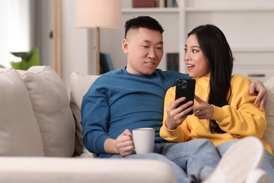 Photo of Happy couple with smartphone on sofa at home