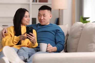 Happy couple with smartphone on sofa at home